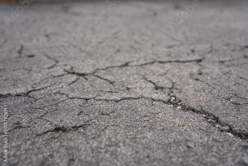 Low angle close-up of cracked grey asphalt texture with selective focus and bokeh