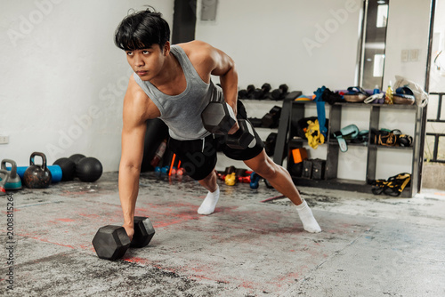 Athletic man performs alternating renegade rows with dumbbells, engaging core and back muscles while maintaining strong plank form in gym.
