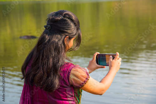 Young girl taking photos of lake on smartphone