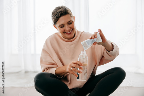 Bild auf Leinwand Hydration comes first as the woman mixes a supplement after workout at home