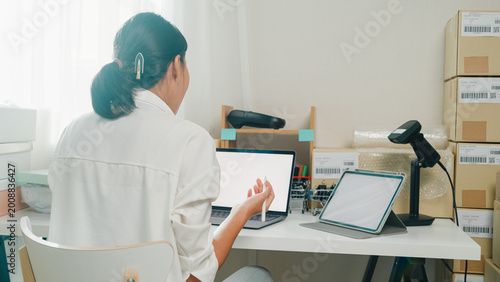 Youth attractive Asia female entrepreneur small business start up call smartphone confirm order with customer confirm check stock inventory product ready for delivery shipment at online retail shop.