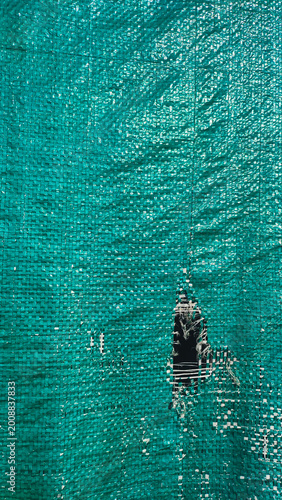 A green tarpaulin covers a structure, displaying a noticeable tear that exposes the area behind it