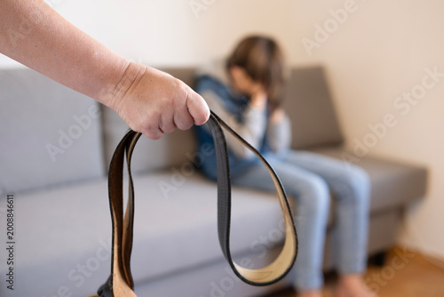 Foto wide leather belt in female parent's hand threatens misbehaving teenage boy sitt
