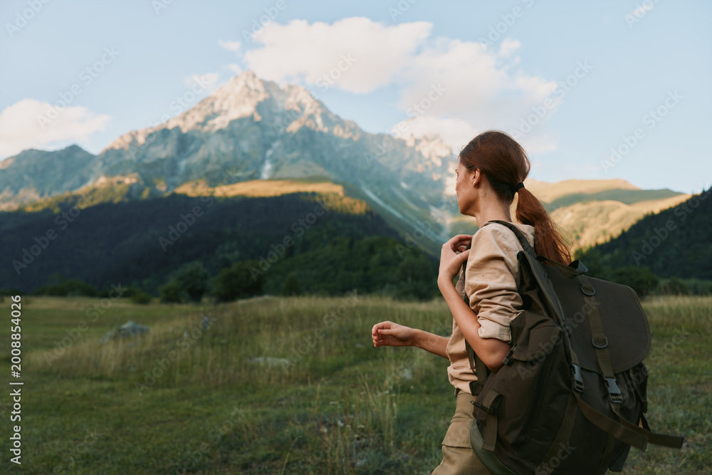 Fototapeta premium Woman hiking with backpack in a grassy meadow before distant mountains, embracing nature and outdoor lifestyle, peaceful landscape and travel vibe