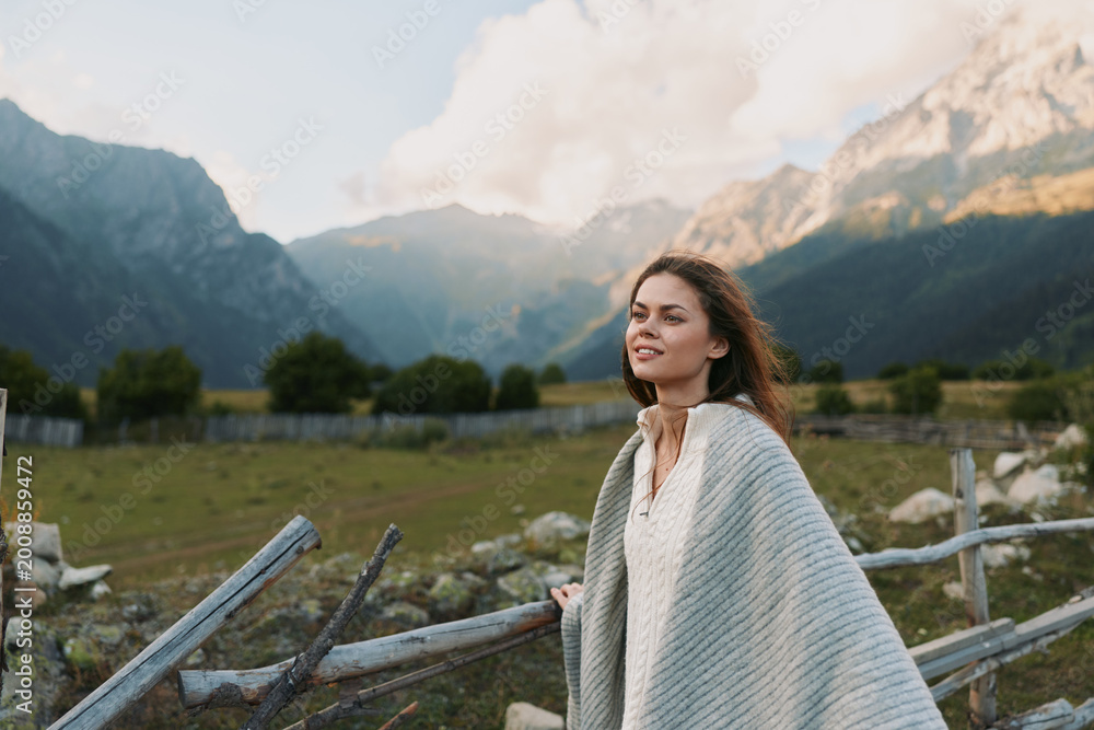 Naklejka premium A woman in a light poncho stands in a mountain meadow, enjoying open sky and fresh air. A tranquil, nature inspired lifestyle moment.