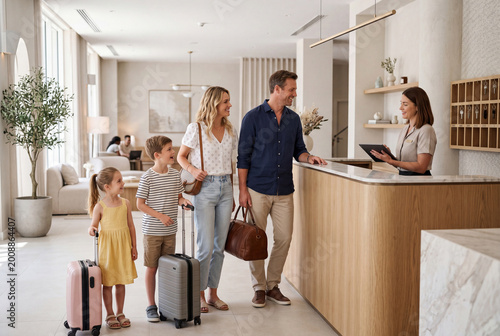 Family checking in at hotel reception with luggage, summer vacation hospitality concept