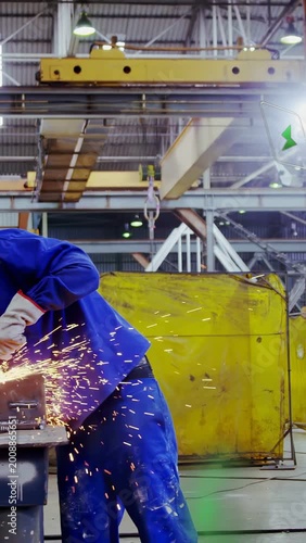 Vertical video: Worker grinding metal in factory, contacting grinder, finishing weld, sparks flying