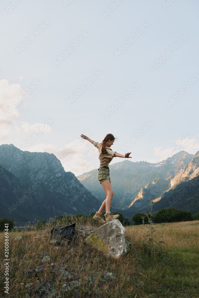 Fototapeta premium Young woman balancing on a large rock in a mountain meadow during daytime. Outdoor lifestyle concept with nature, adventure, and freedom in a scenic landscape.