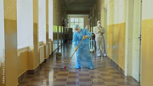 Sanitary worker cleaning a hospital corridor in full protective hazmat suit.