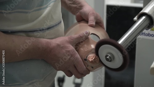 Skilled technician carefully uses a specialized rotary grinding tool to smooth and finish the fitting socket of a custom-made prosthetic limb during manufacturing process.
