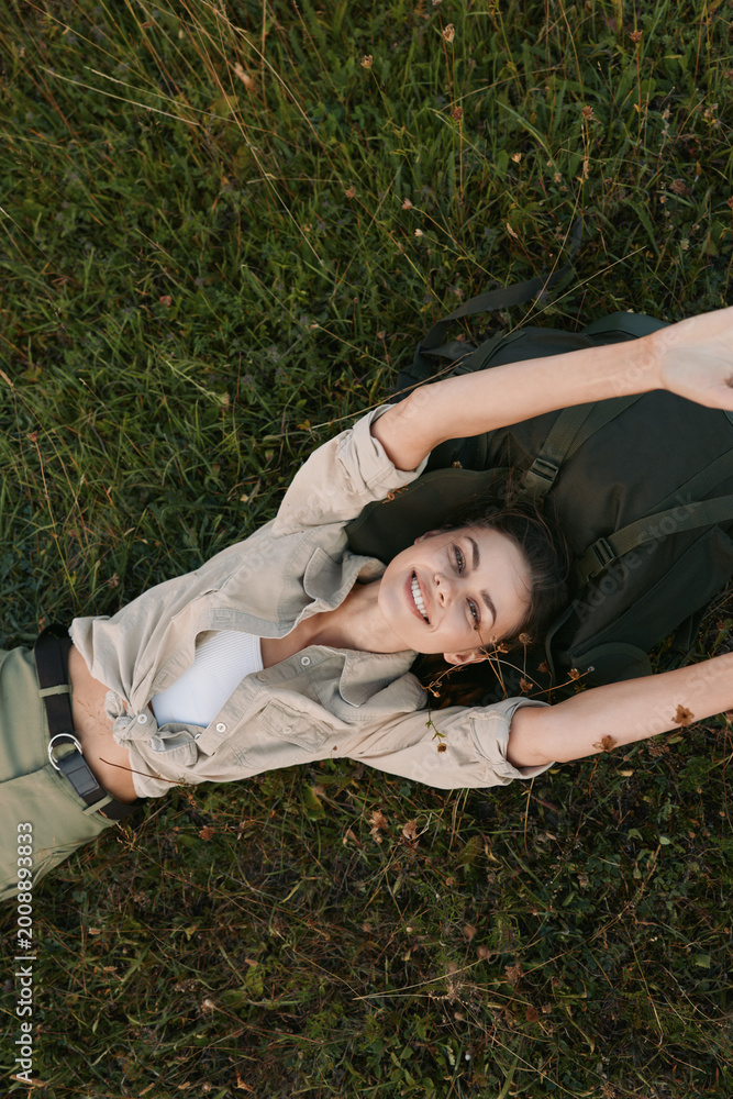 Fototapeta premium Relaxed woman lying in tall grass, arms stretched above her head, enjoying a carefree outdoor moment. Natural light creates a warm, peaceful mood and wellness themes.