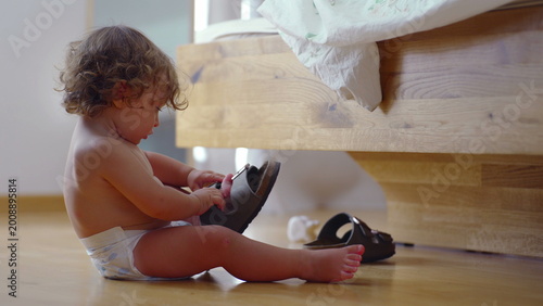 Photos Toddler sitting on bedroom floor trying to open sandal buckle, focused explorati