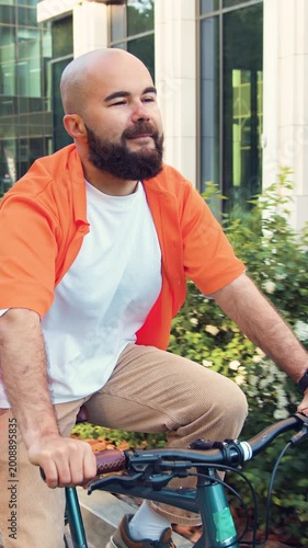 Stylish hipster man riding on vintage bicycle. Caucasian guy in smart casual outfit riding bike along urban wall on city street while going to office in the morning. Slow motion.