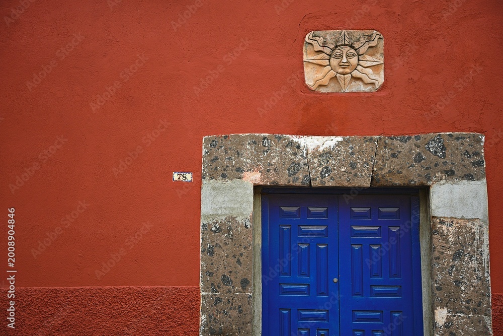 Obraz premium Old Colonial house blue wooden door with stone trim on a Venetian red stucco wall in San Miguel de Allende, Guanajuato Mexico.