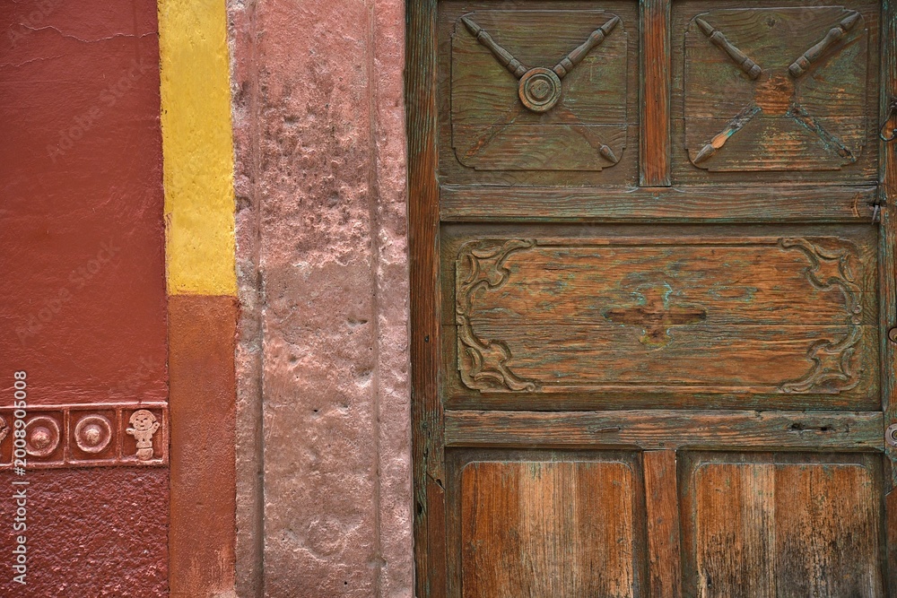Fototapeta premium Old Colonial house facade with a Venetian stucco wall and an antique hand carved solid oak wooden door in San Miguel de Allende, Guanajuato Mexico.