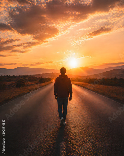 Journey into the Sunset: A lone figure walks along an open road towards a blazing sunset, symbolizing the path of life, hope, and the pursuit of dreams. The vibrant colors paint a picture of solitude.