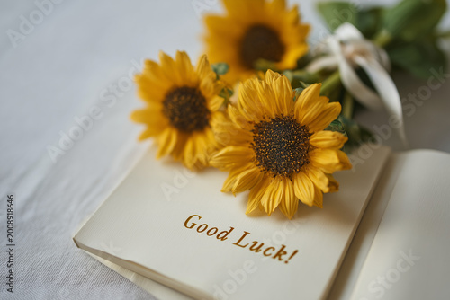 Open Book with Sunflowers and Good Luck Text Top View Soft Focus Floral Composition