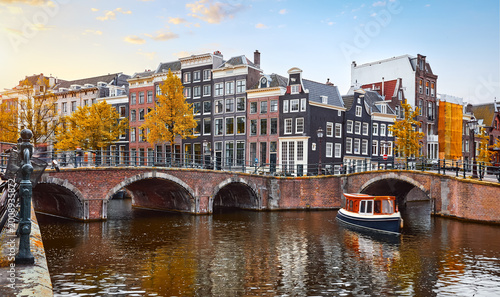 Amsterdam Netherlands. Traditional dancing houses on the river Amstel channel. Pleasure boat under the bridge. Sunset time. Popular travel destination in Europe