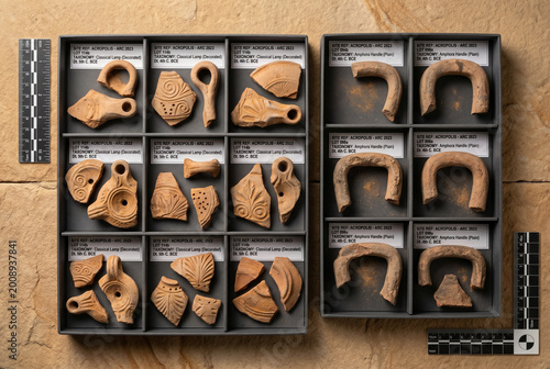 Various ancient pottery pieces are arranged neatly in trays. Each piece shows unique designs and forms. The trays are labeled with Descriptions and dates.