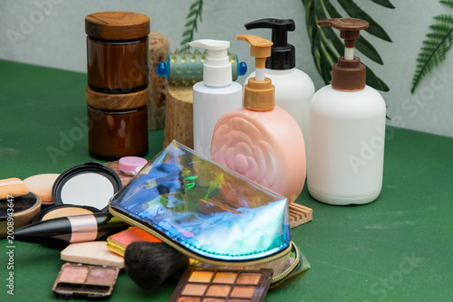 Scattered Makeup Collection with Iridescent Bag, Eyeshadow Palette, and Beauty Products Cosmetic on Green Surface