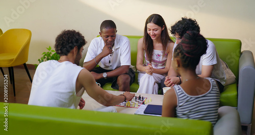 Indian young adult gen z male female group team sitting on sofa couch play chess indoor room place teen girl boy look game watch match talk speak share idea spend break time enjoy new day have fun joy