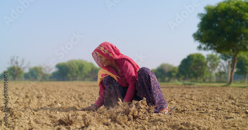 Foto Indian elderly mature villager lady woman sitting field do work dry tilled soil residue outdoor rural area