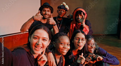Indian young adult gen z male man female look camera take selfie photos have fun joy hall stage place. Happy teen girl boy group team staring cam do funny pose record video spend day enjoy break time