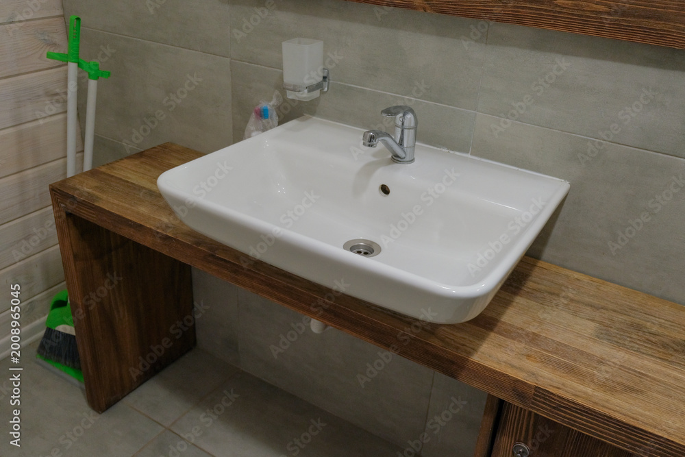 Fototapeta premium Modern faucet and water flow. Stylish white sink in a light interior. Chrome steel tap. Domestic Appliances. Gray clean bright bathroom. Household equipment. Grey vanity with tiled wall. Home interior