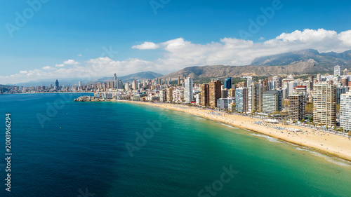 Drone shot majestic Benidorm skyline Costa Blanca. Panoramic view of skyscrapers on seashore with mountains behind. Bright sunny spring weather spanish tourism architecture scene.