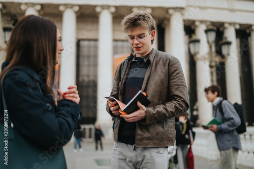Tableau sur toile A male student reads notes from a notebook while talking with a classmate outside