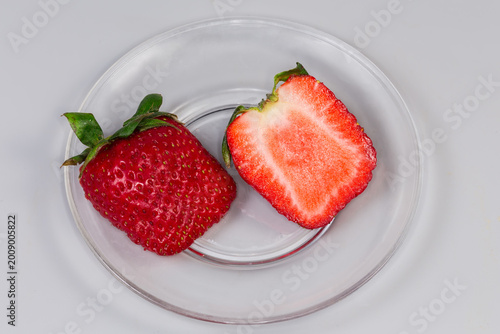 Fotografie Halved freshly harvested garden strawberry with sepal on glass saucer
