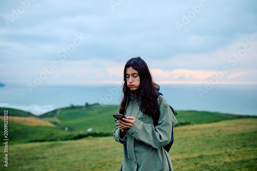 Foto Young woman standing on a green hill overlooking the sea, feeling bored and dist