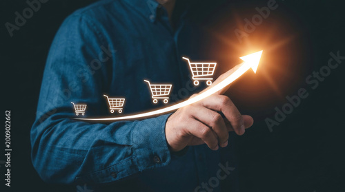 E-commerce sales growth concept, businessman pointing at rising arrow with shopping cart icons, retail marketing success and financial profit increase