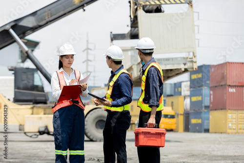 Three workers in safety gear discuss logistics at a busy shipping port with containers and heavy machinery in the background.