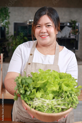 Fresh green salad bowl held by a happy woman in a kitchen setting. Healthy eating and vegan lifestyle. Concept of eating to lose weight.