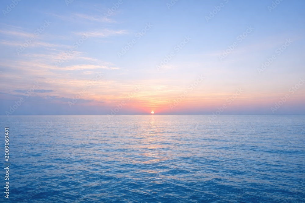 Obraz premium Serene ocean horizon at sunrise with soft pastel colors in the sky and calm blue water reflecting the morning light over the sea