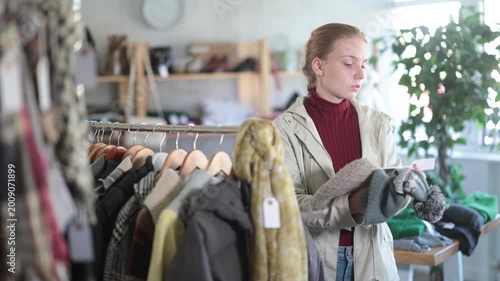 While shopping, teen girl browsing goods items and choose elect hat in store, buyer consider some items. Concept of seasonal wardrobe shopping. Client and holiday shopping.