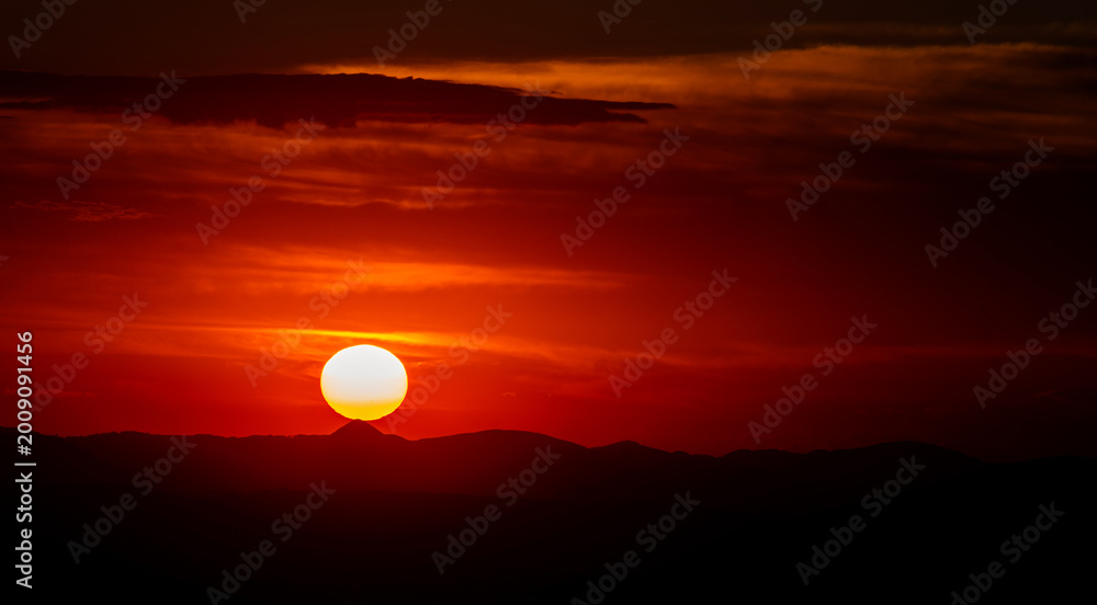 Fototapeta premium Dramatic Mountain Sunset with Clouds and Visible Sun Disk