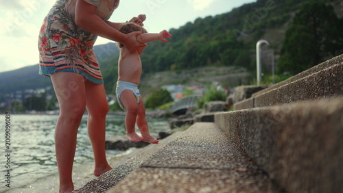 Fotografía Toddler crying while mother holds him back from touching stone steps near lake,