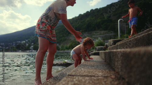 Fotografía Toddler crying while mother holds him back from touching stone steps near lake,