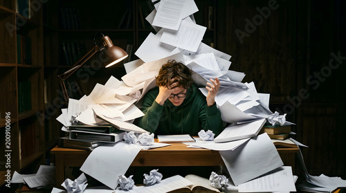 stressed student overwhelmed by exam paperwork under dim desk lamp at night