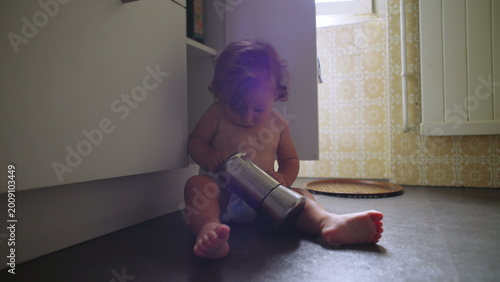 Fotografía Toddler sitting on kitchen floor playing with metal coffee pot, deeply focused a