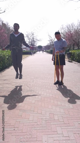 Two young athletic men exercising outdoors on a sunny day. An african american man is jumping rope and an asian man is using a resistance band