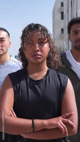 Multiracial athletic friends looking at the camera outdoors. Woman in front crosses her arms and smiles while men stand behind her