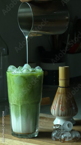 Homemade style of person pouring fresh milk over matcha green tea to make a matcha milk latte, delicious drink to enjoy at home. Vertical photo