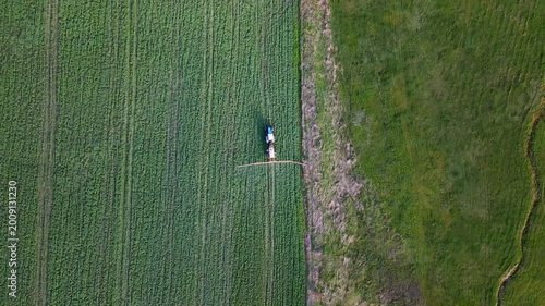 Aerial top view of tractor spraying fertilizer on green agricultural field.