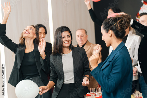 Business party celebration with diverse adult worker group dancing and smiling in office interior, joyful social gathering