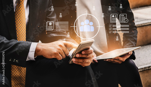 Obraz na płótnie Two business professionals collaborate using a smartphone and tablet, surrounded by digital graphics representing teamwork and data in a modern work environment