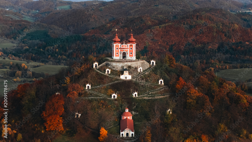 © AmazingAerialAgency - Aerial view of the Kalvaria Banska Stiavnica complex on a hill surrounded by autumn forests in Banska Stiavnica, Banskobystricky kraj, Slovakia.