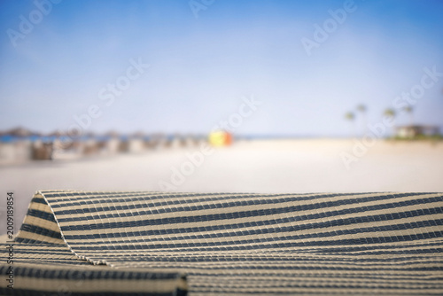 Minimal summer composition featuring clean sandy beach with empty copy space for product placement. Rocky coastline meets the sea under bright blue sky, creating natural and scenic atmosphere.